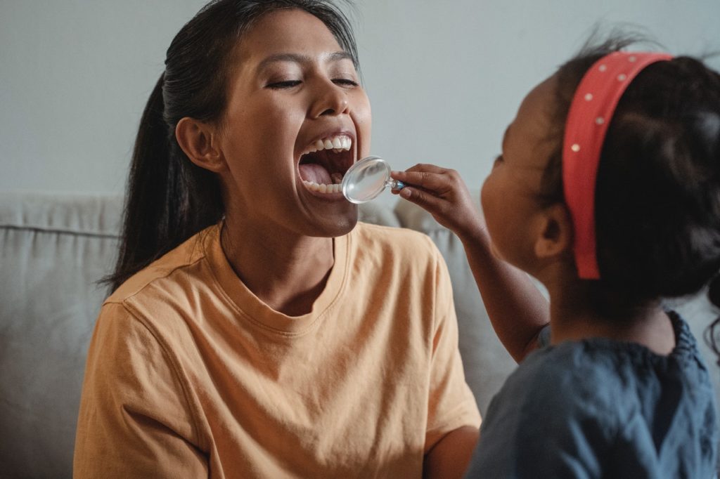 A child looks at her mother’s dental crowns with a magnifying glass.