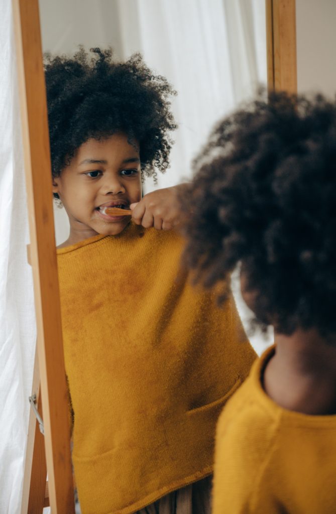Young child brushing teeth in a mirror.