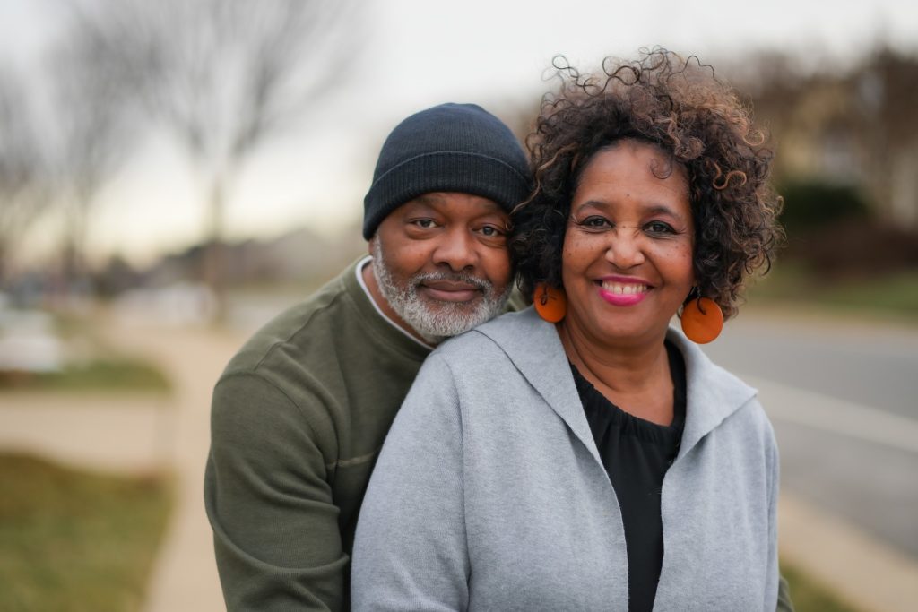 An older man and woman smiling while standing on a sidewalk