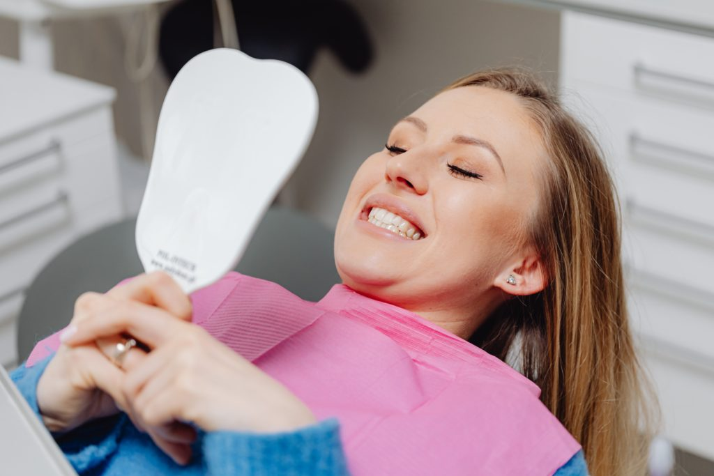 woman holding small mirror and looking at her clean teeth