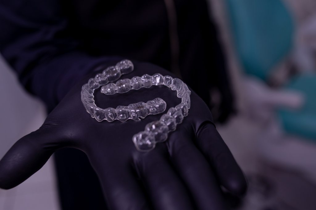 person holding invisalign aligners with black gloves