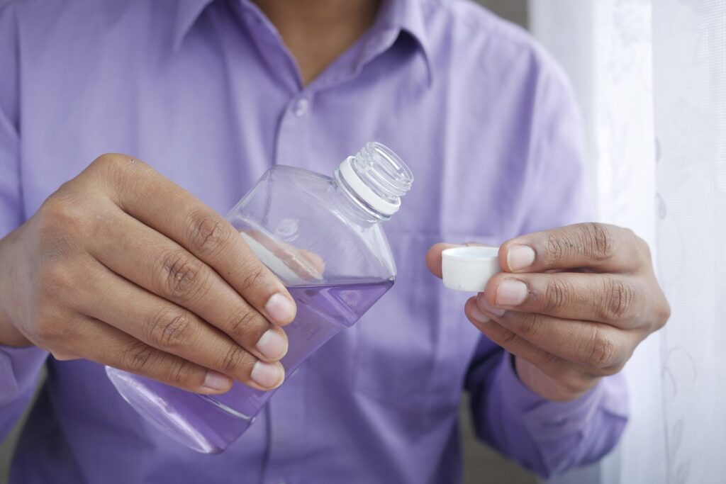A person’s hands holding a bottle of mouthwash and the bottle’s cap