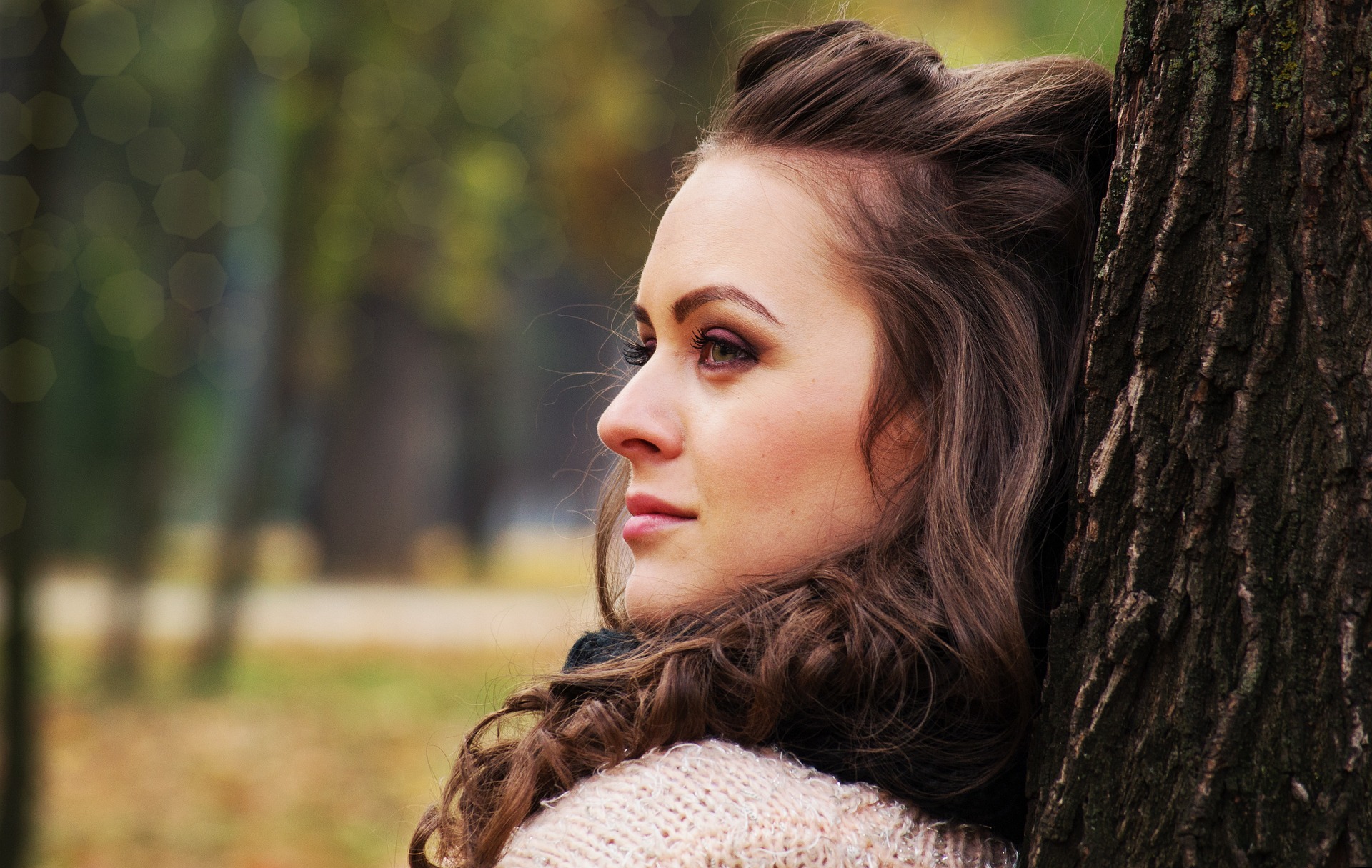 A woman leaning against a tree and looking off to the left