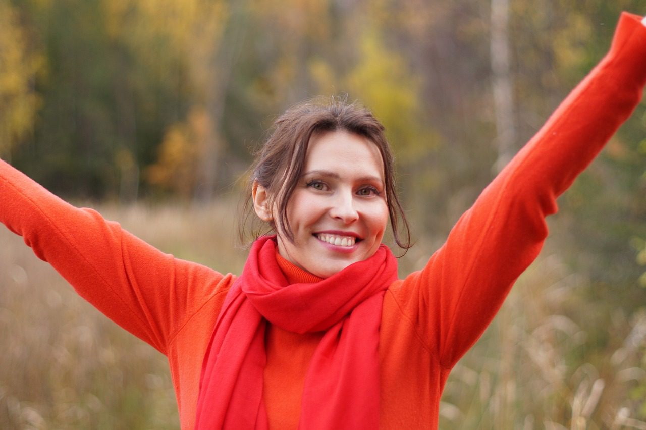 woman in orange smiling with arms raised